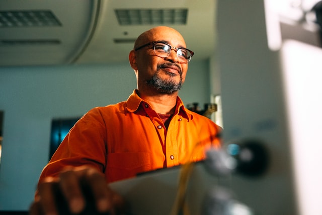 A man in an orange shirt smiles at a computer screen